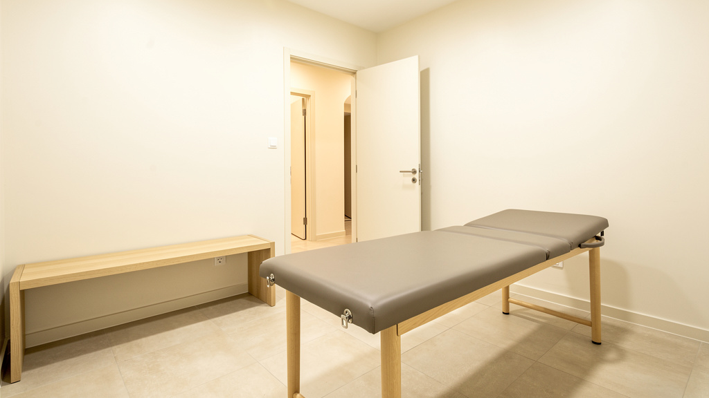 A calm open recovery area with a padded table and an oak bench along the wall