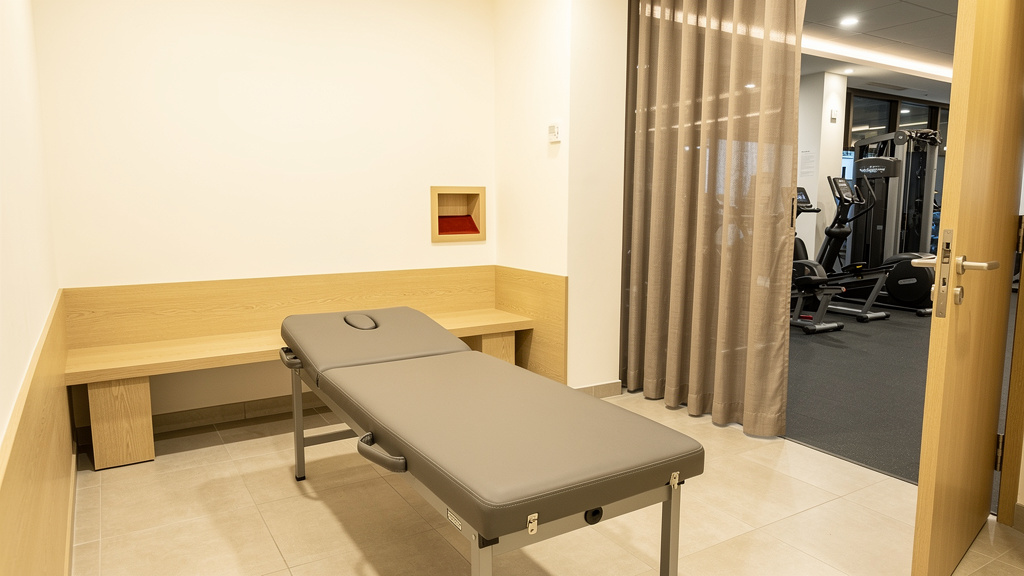 A curtained corner of a gym floor with a padded table and a pale oak bench, nobody present