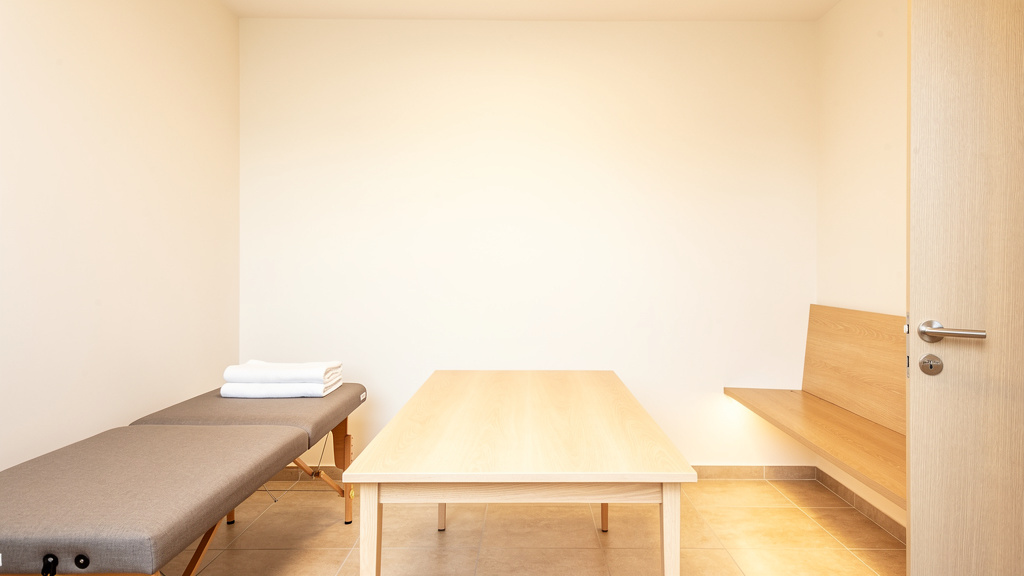 A calm recovery room with a padded table and a pale oak bench against the wall, even warm light