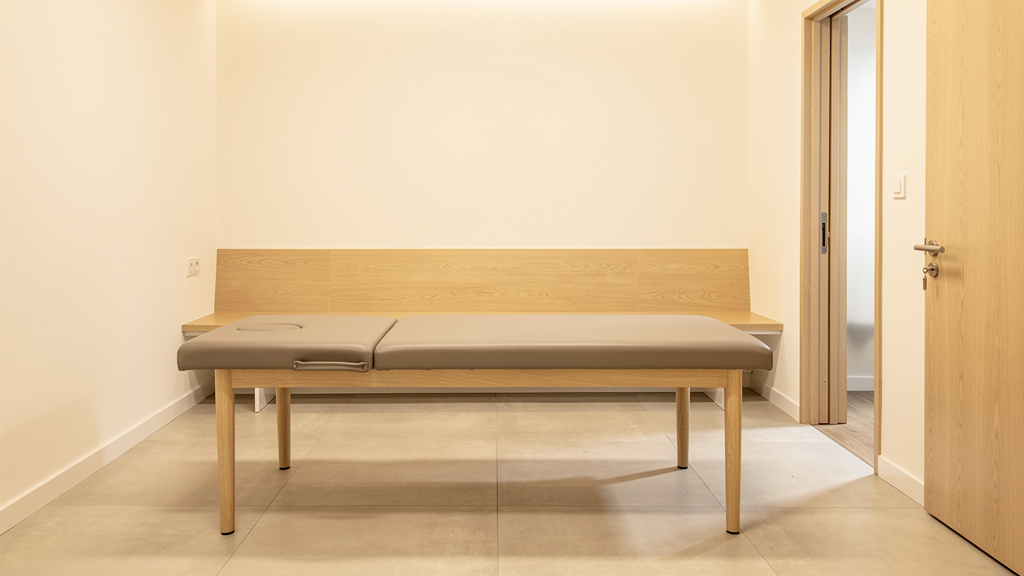An empty recovery room, a padded table at its centre with nothing standing beside it, door open