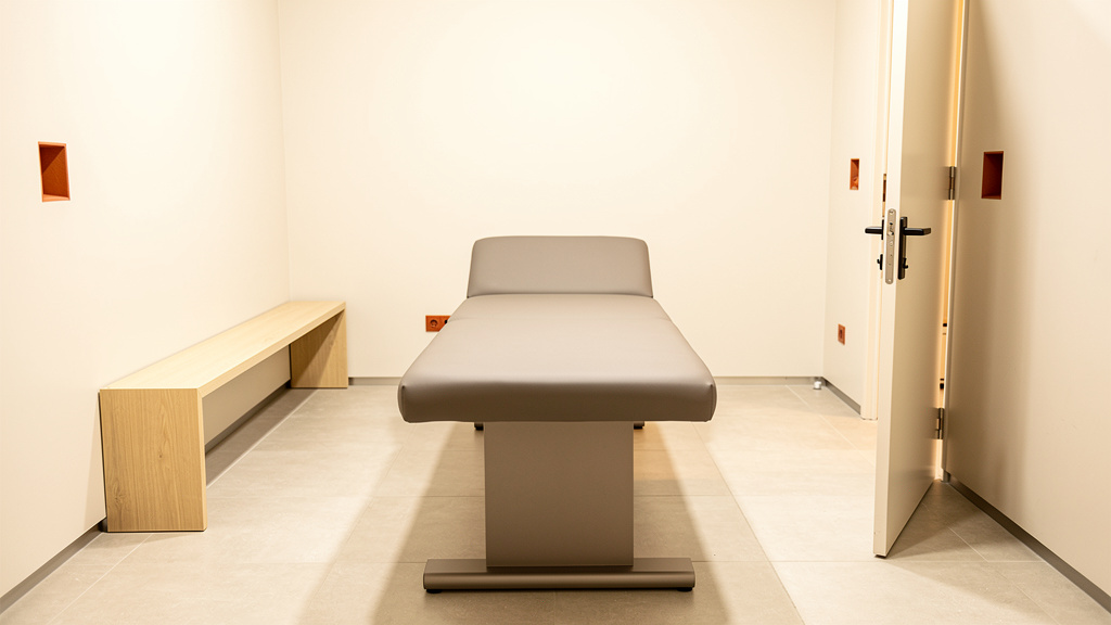 A calm recovery room with a padded table in warm grey, door open