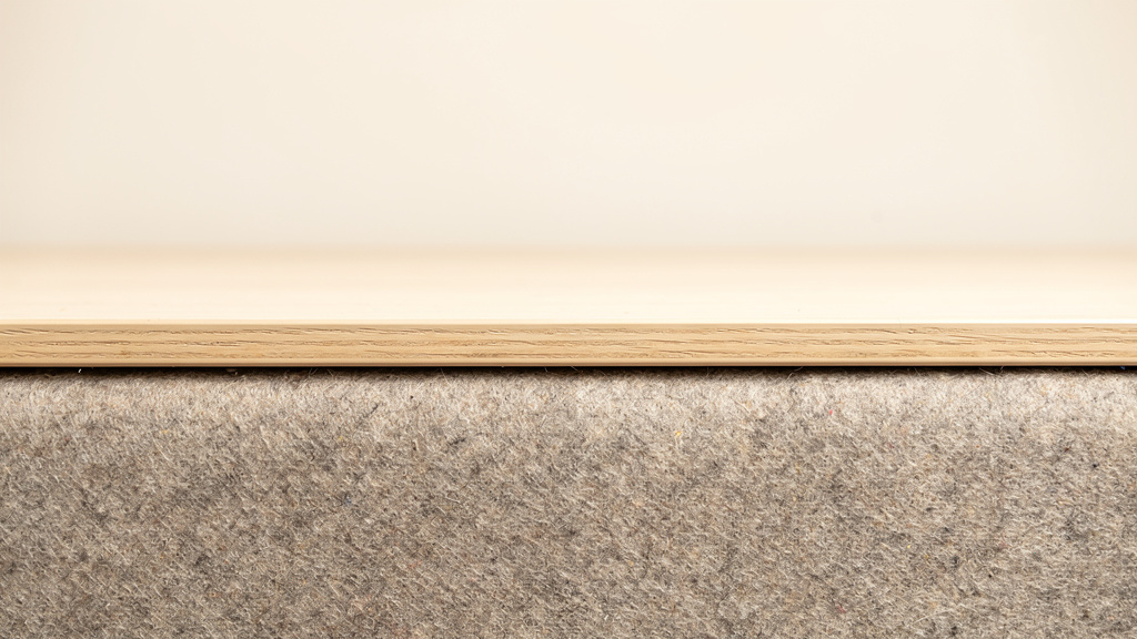 A pale oak table top meeting a warm grey felt surface, edges precisely aligned